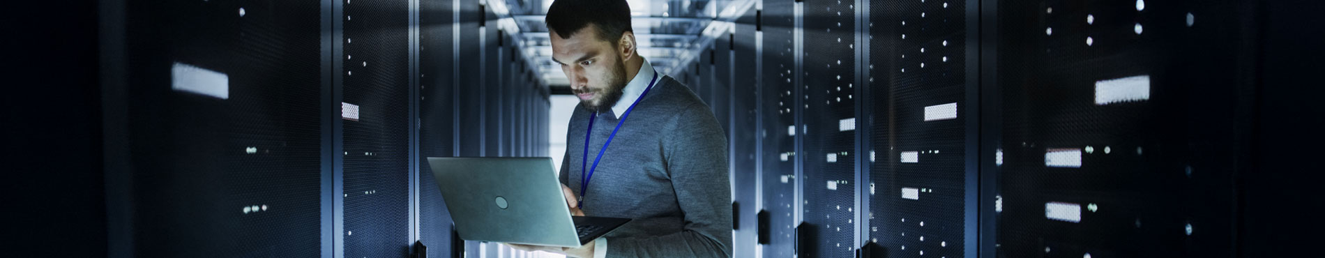 Ein Mann in einem Rechenzentrum arbeitet konzentriert an seinem Laptop zwischen Serverregalen.