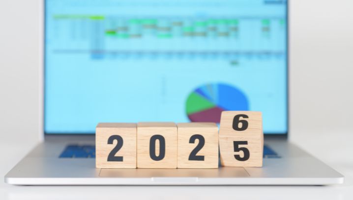 Holzwürfel mit den Zahlen 2025 und 2026 vor einem Laptop mit Diagrammmuster, symbolisiert Neuanfang und Planung.