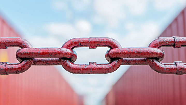 Rote Kette vor unscharfen Containern. Stärke und Halt vermitteln ein industrielles Flair.